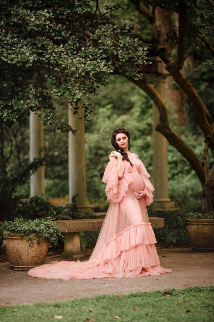 pregnant woman in tulle blush gown standing in front of Cator Wollford Gardens stone colonnade in Atlanta, GA