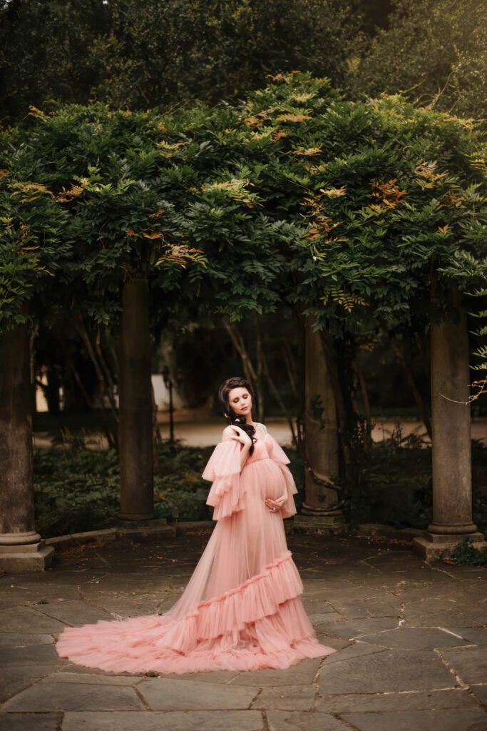 Pregnant woman in a blush tulle gown with the Cator Woolford Gardens colonnade in the background in Atlanta, GA.
