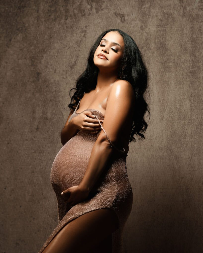 Pregnant black mom in a sheer gown with strap falling off her shoulder and eyes closed cradling her belly