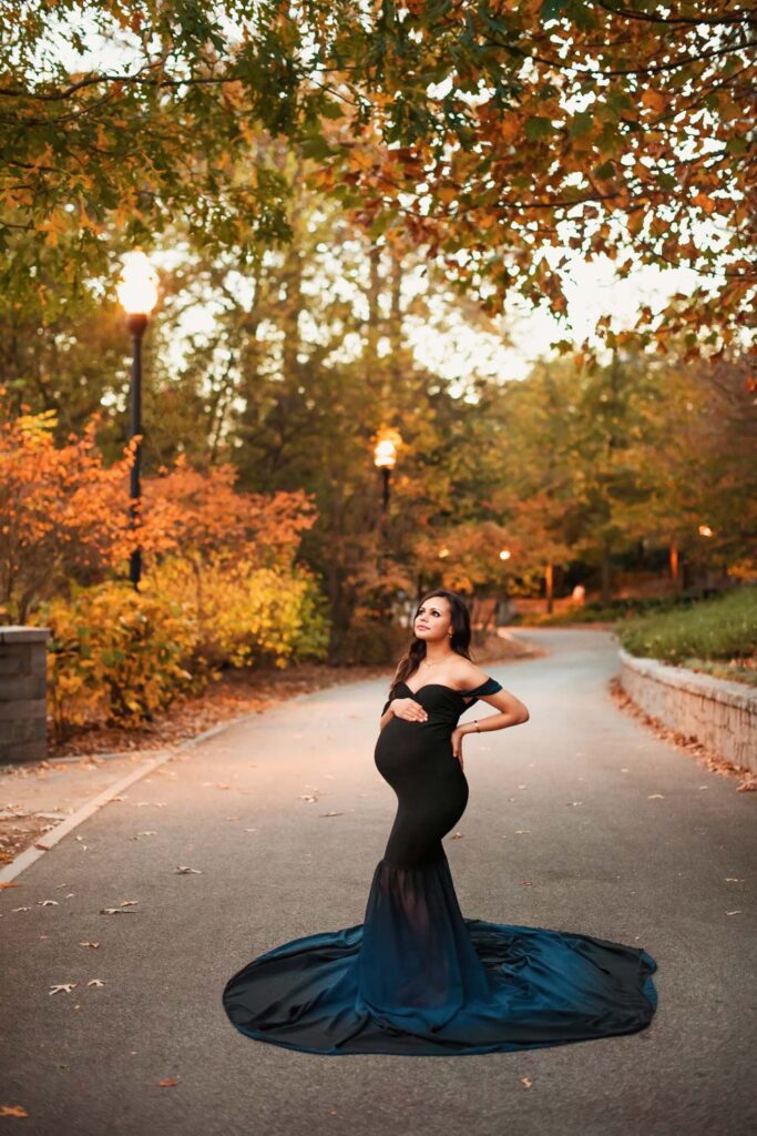Maternity photoshoot of pregnant mom wearing black and blue mermaid style dress on winding path with street lamps.