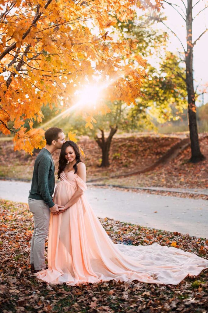 Couple stands beneath bright orange fall leaves during Atlanta maternity photos at Piedmont Park