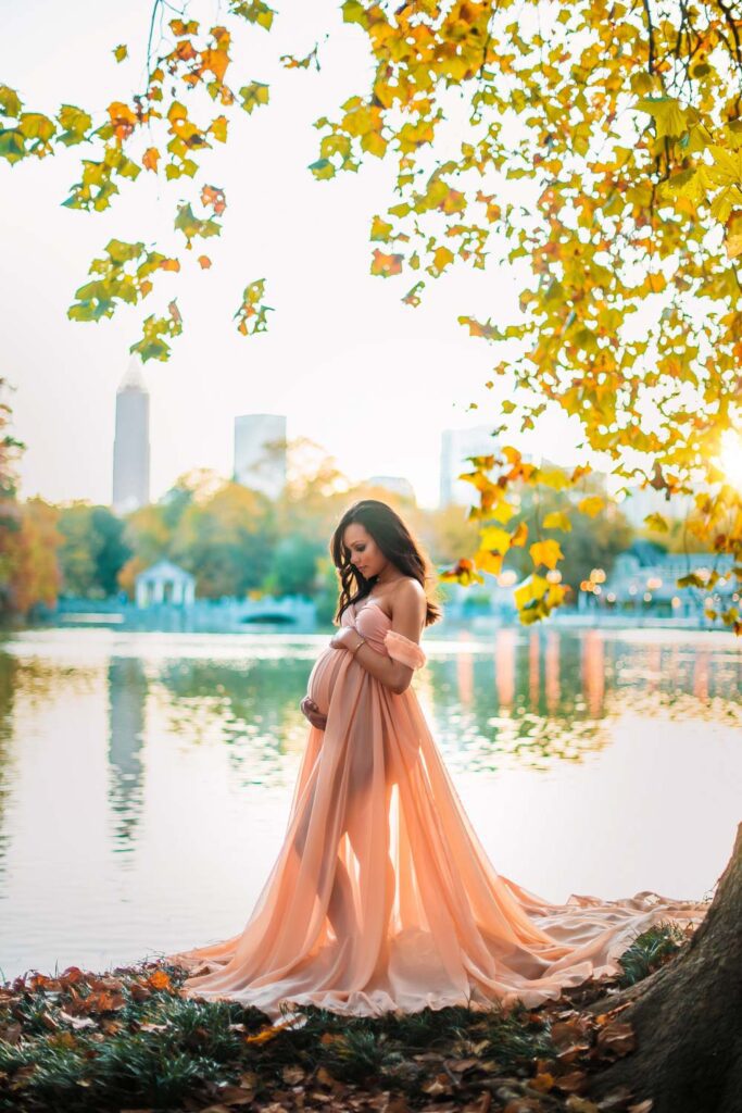 pregnant woman in sheer dress with Lake Clara Meer and Midtown skyline in the background at Piedmont Park in Atlanta, GA.