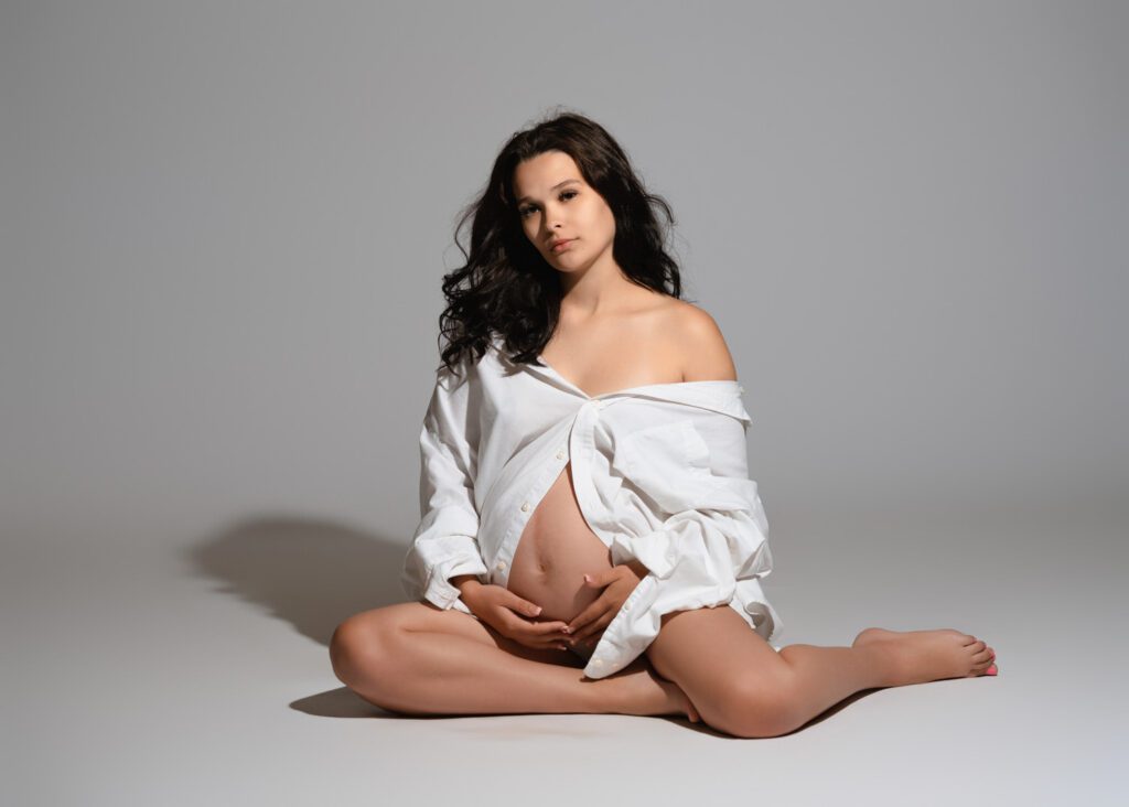 pregnant woman siting on studio floor in a white shirt during a professional maternity portrait session