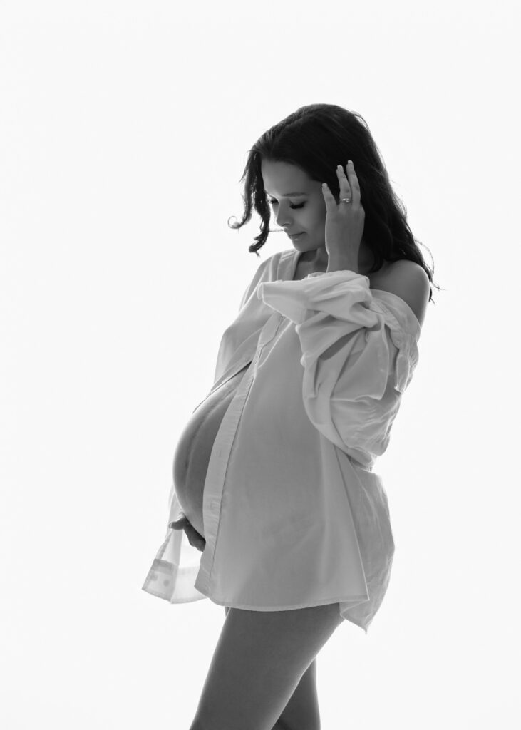 Expecting mother in a white robe cradling her belly during a maternity photography session