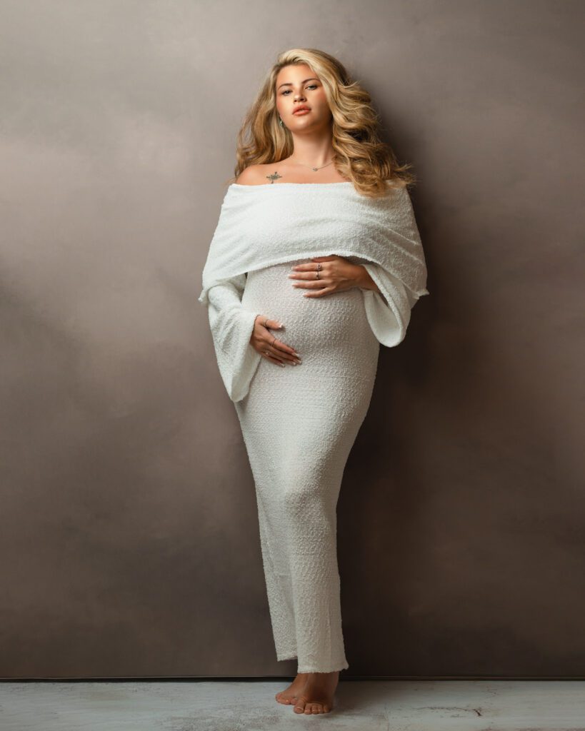 Expecting mother in a white gown leaning on wall photographed by Sandy Springs maternity photographer.