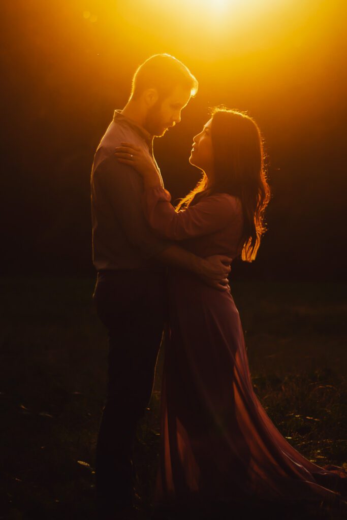 Mom and dad embracing in silhouette as intense golden sunset light shines behind them.