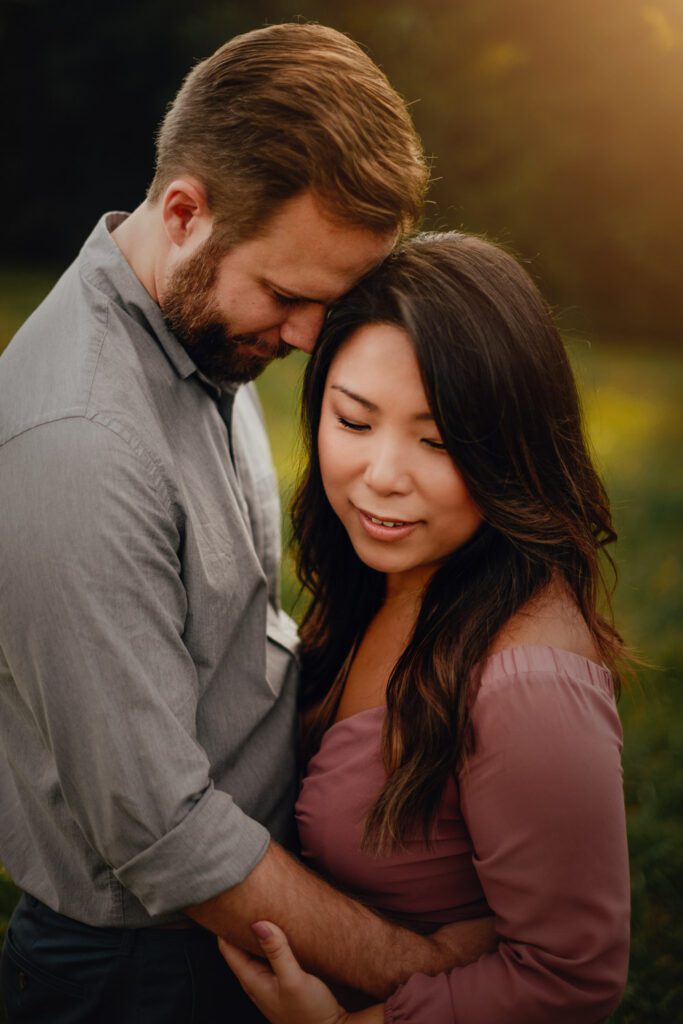 Mom and dad embracing closely in meadow at sunset