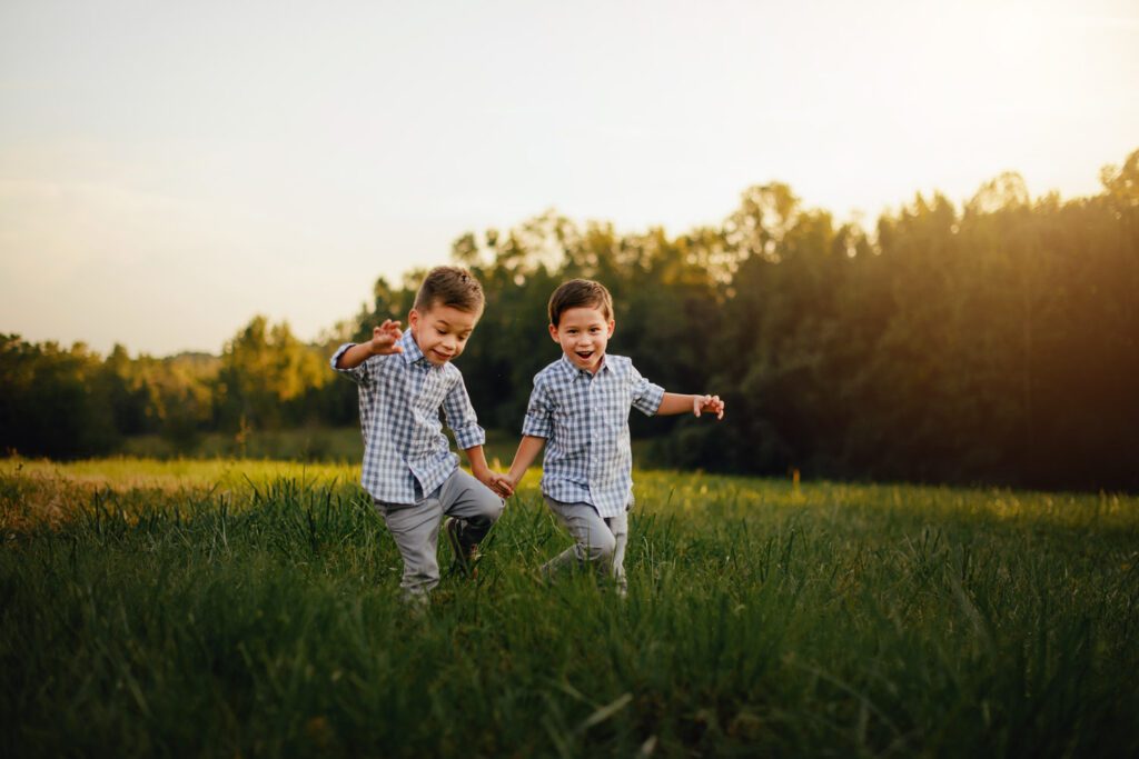 brothers holding hands and running through a tall grass field at golden hour sunset in Alpharetta GA