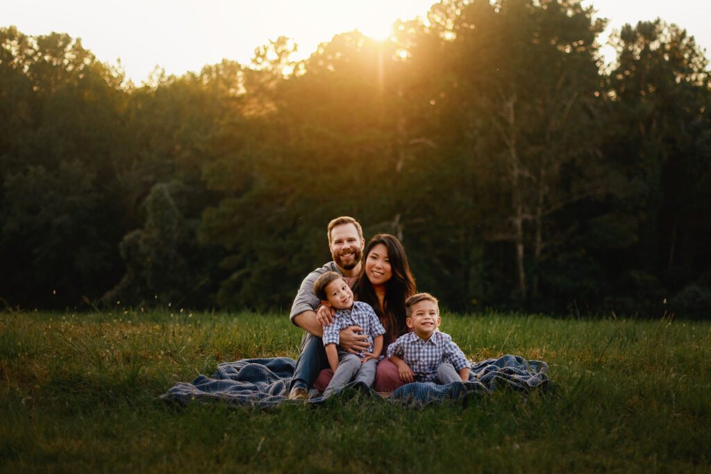 Family sitting together on a blanket with Garrard Landing Park tall grass meadow in the background in Alpharetta, GA.
