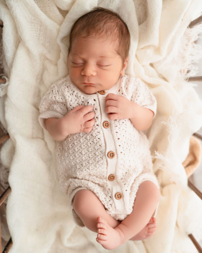 Sleeping newborn baby in a vintage wooden cradle with soft window light shining through white curtains.