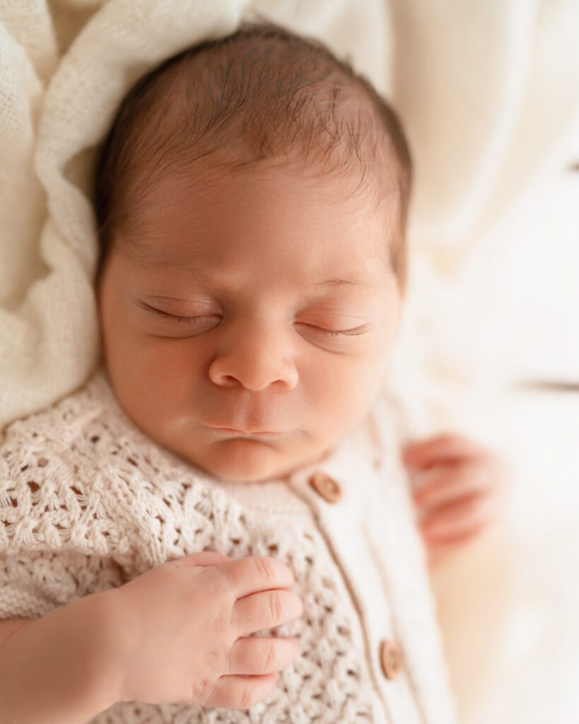 Newborn baby in white knit romper sleeping peacefully on blanket during a studio photoshoot with an Alpharetta newborn photographer.