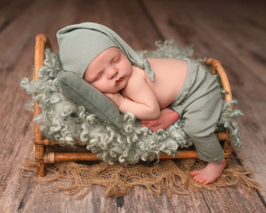 Newborn baby boy curled on his side in a blue romper with a knit teddy bear during Atlanta newborn photos.