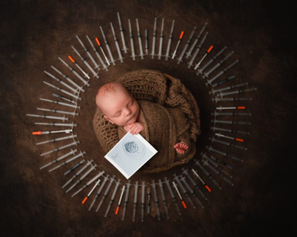 Atlanta IVF newborn portrait of a baby boy holding his embryo transfer photo surrounded by IVF syringes.