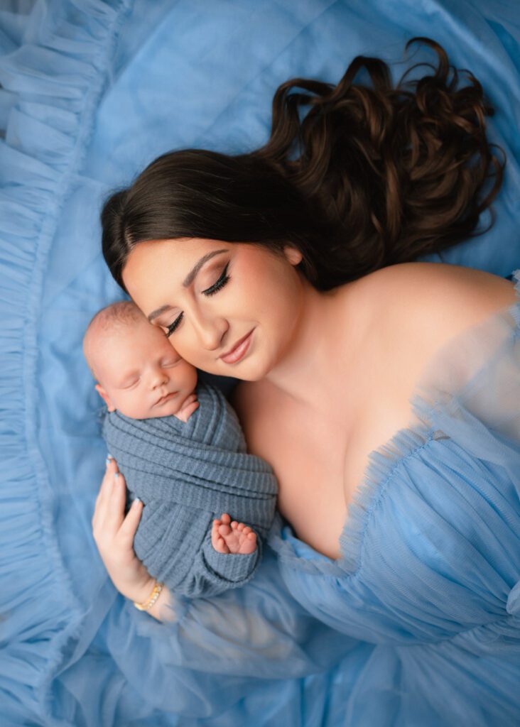 Mom in a sky blue tulle dress lying beside her swaddled newborn baby boy during an Atlanta newborn session.
