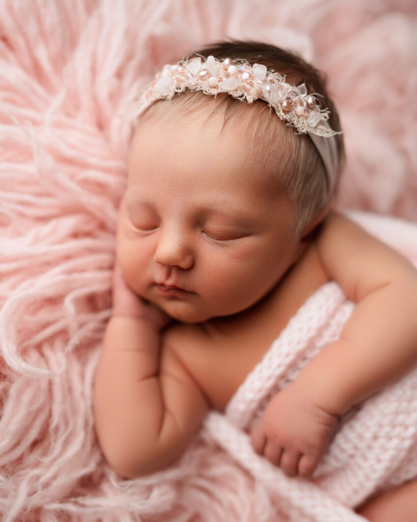 Baby girl sleeping with her head on her hands in a pink beaded headband and crochet wrap