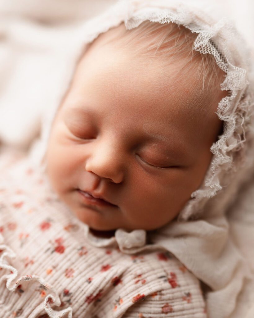Sleeping newborn baby girl in a lace bonnet resting on a cream blanket during an Atlanta newborn session.