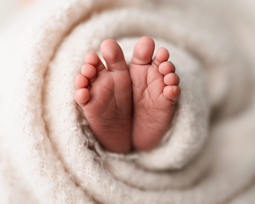 Close-up of a newborn baby girl’s feet bundled in a soft pink blanket, showing her tiny toes and wrinkles.