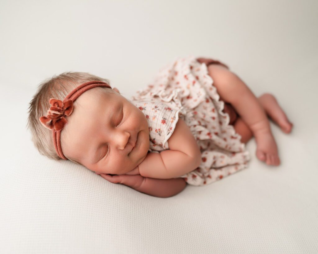 Newborn baby girl sleeping on her side in a floral outfit on a cream blanket for Atlanta newborn photos.