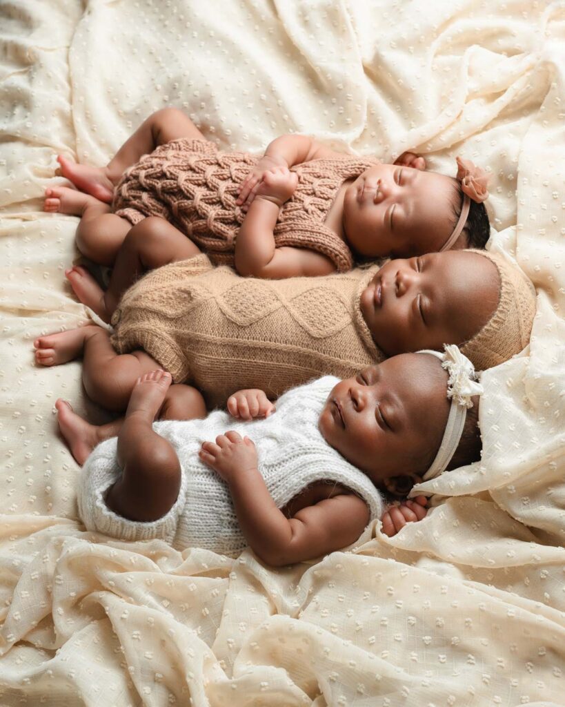 Triplet newborn babies lay together on a beige fabric wearing textured knot outfits in blush, tan and white. 