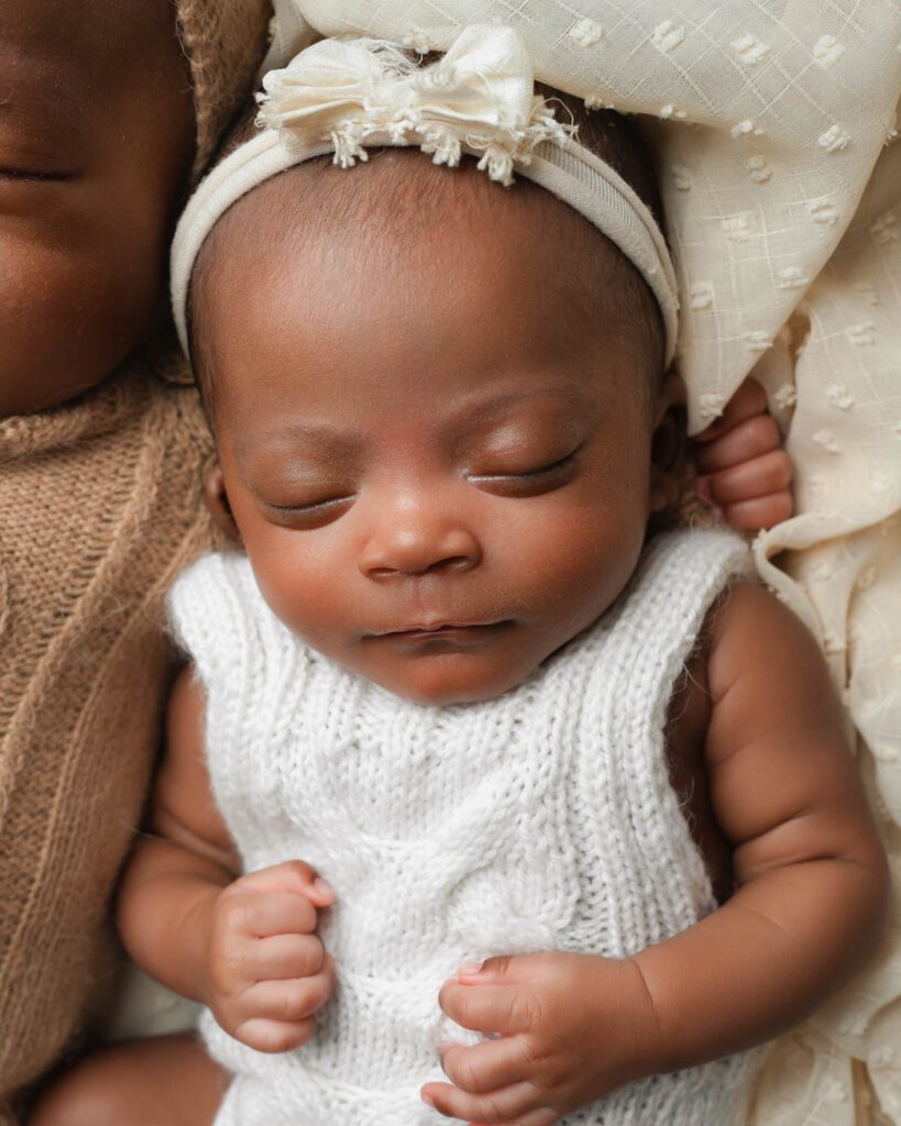 Baby girl in a white knit romper and bow headband beside her brother during Atlanta triplet newborn photos.