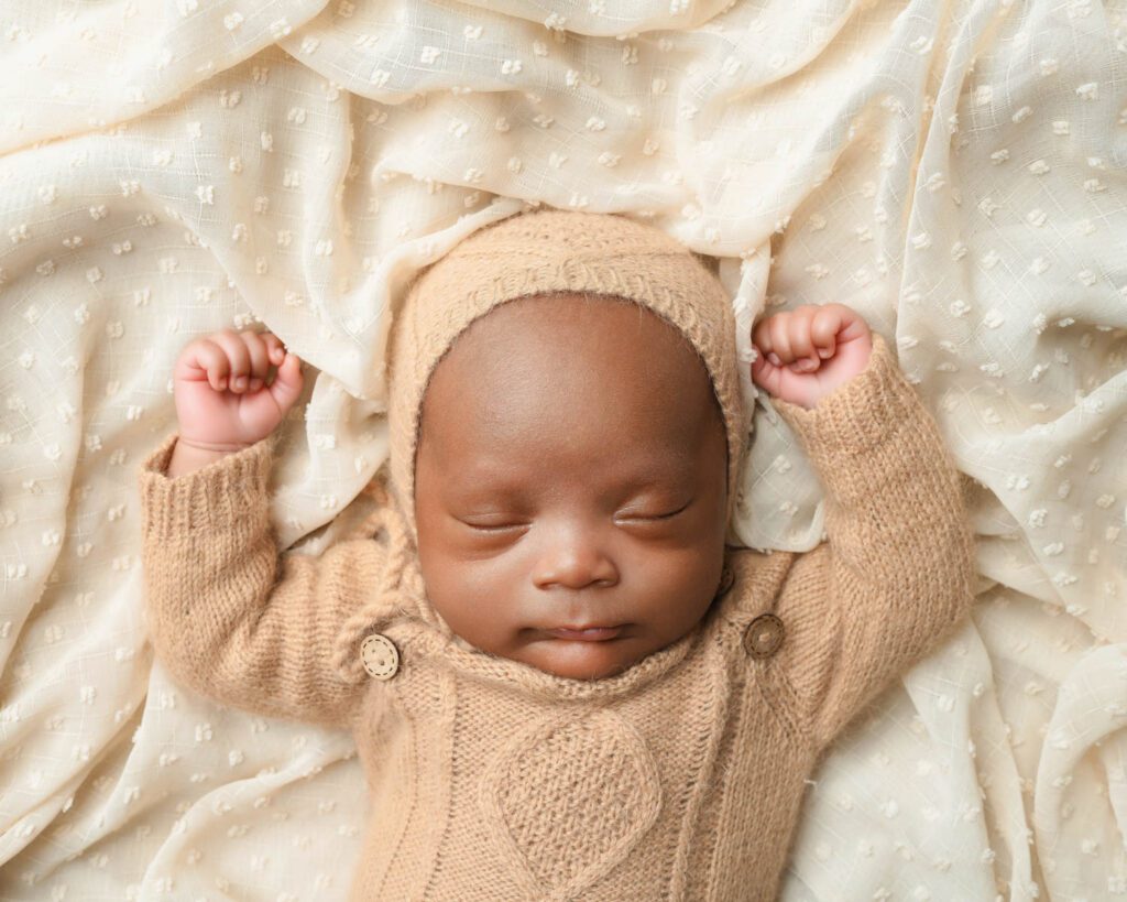 Sleeping newborn baby boy in a tan knit outfit with both arms raised during an Atlanta triplet newborn session.