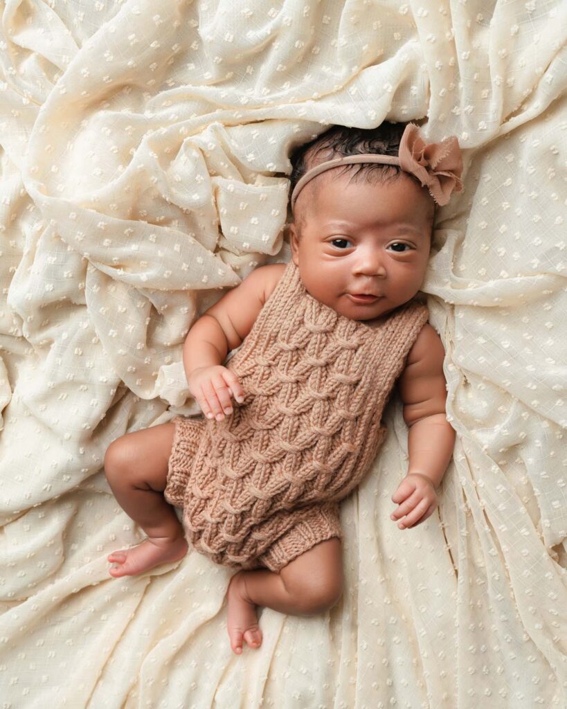 Alert baby girl in a brown knit romper and bow headband looking at the camera during an Atlanta newborn session.