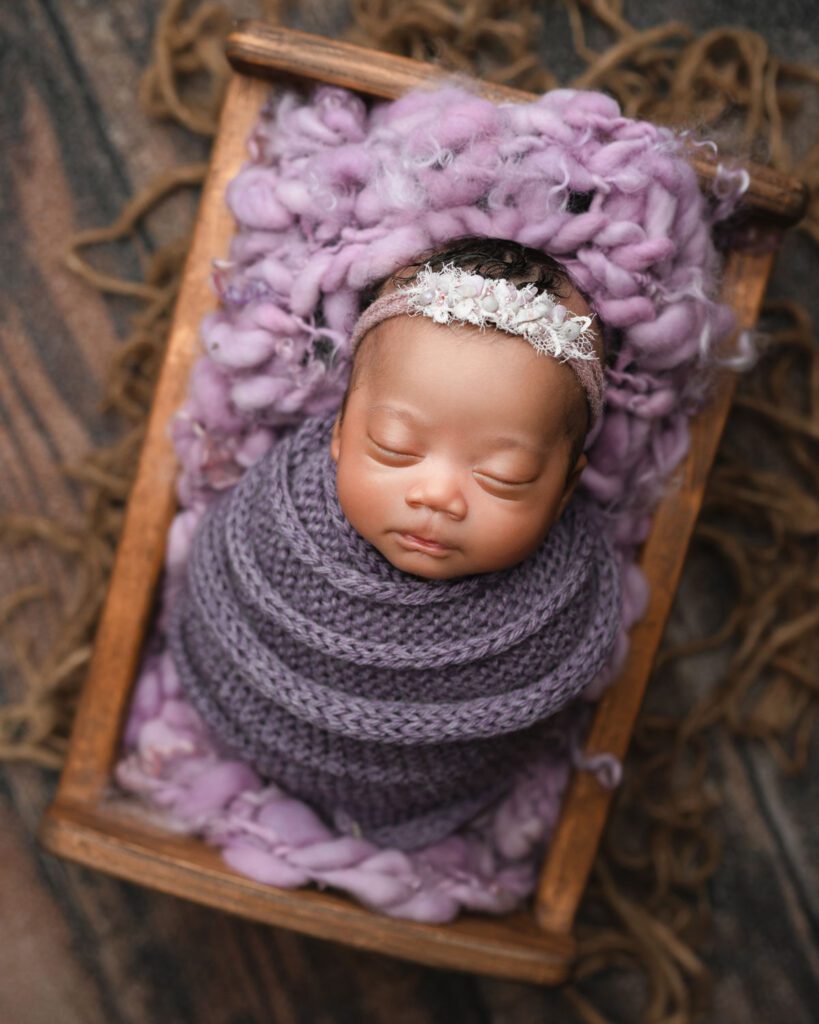 Sleeping newborn baby wrapped in purple with a matching knit bonnet during triplet newborn photography.