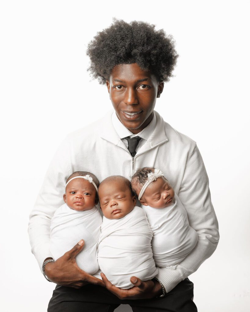Dad holding all three swaddled babies in his arms during triplets newborn photos.