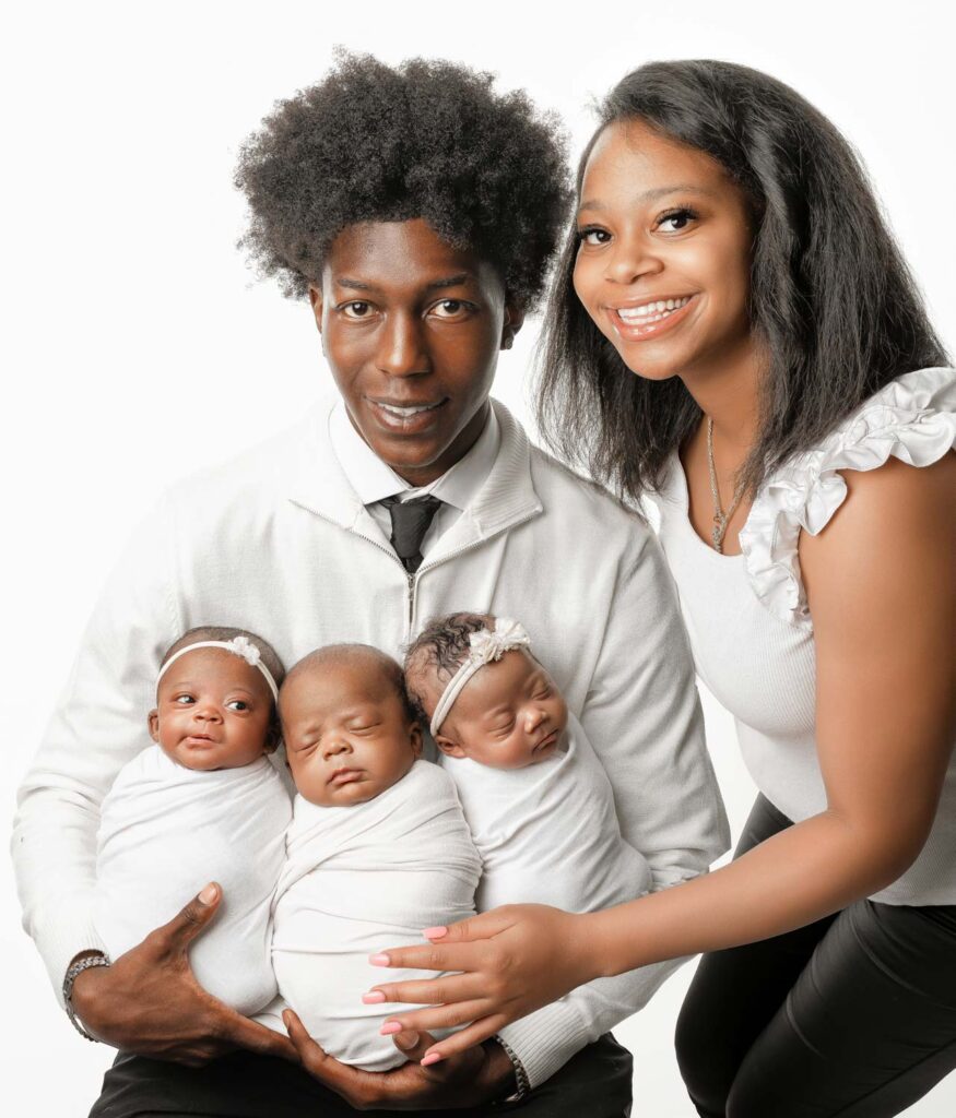 Parents posing with their three swaddled newborn babies during a triplet newborn photo session.
