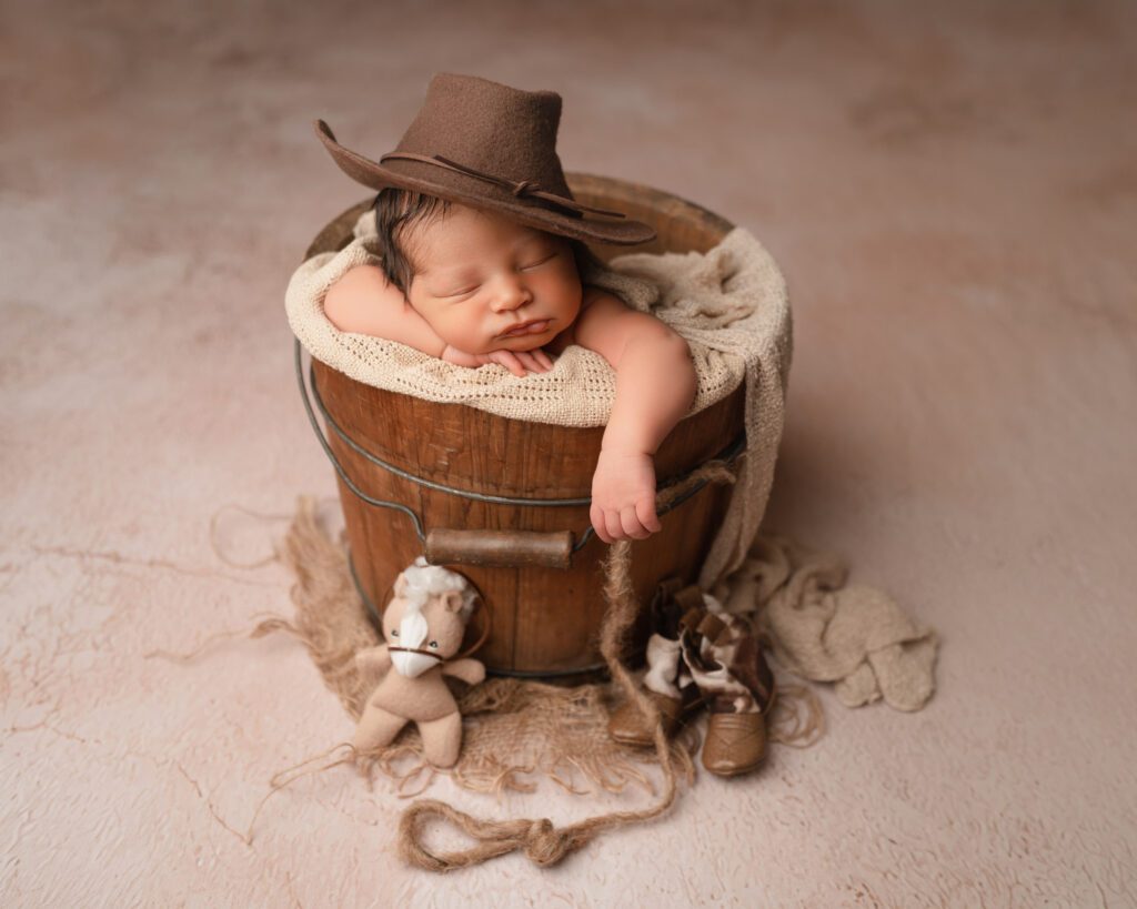 Newborn baby boy sleeping in a wooden bucket with a cowboy hat for a Buckhead newborn photographer.