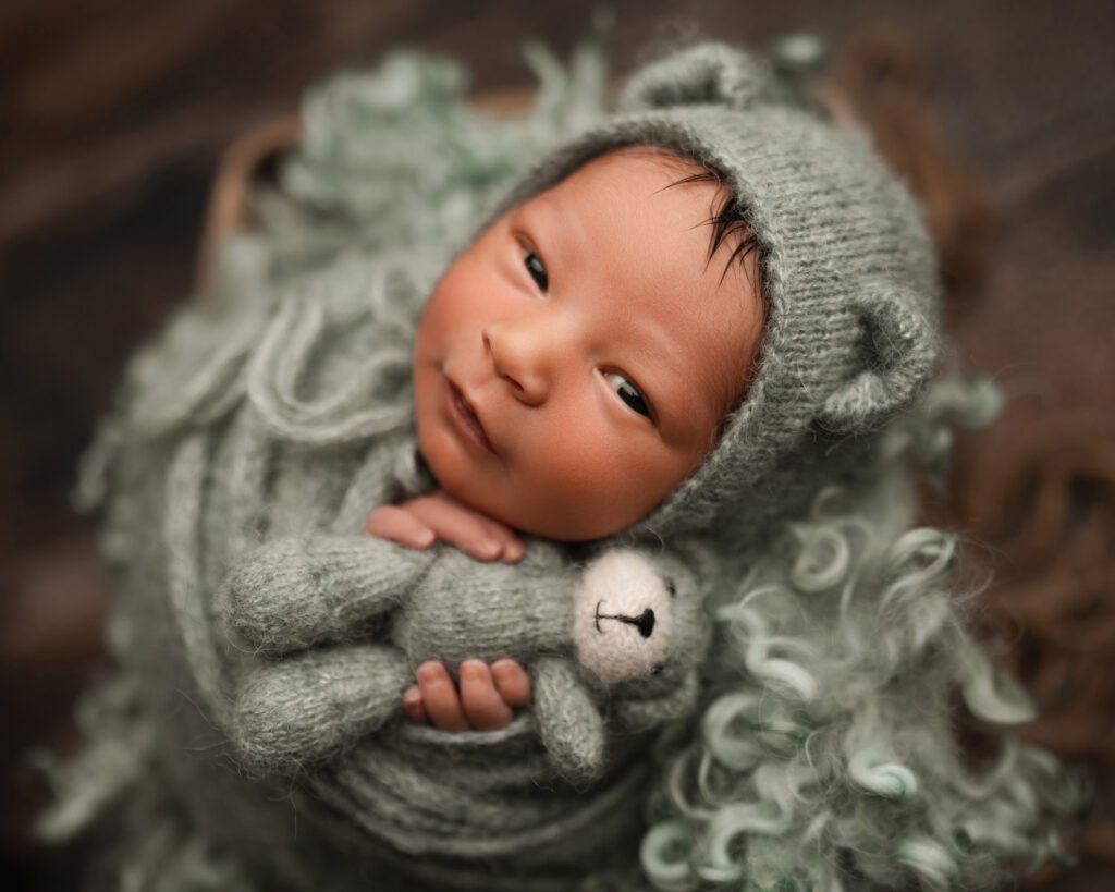awake baby boy wrapped in soft sage knit with a tiny bear, looking toward the camera.