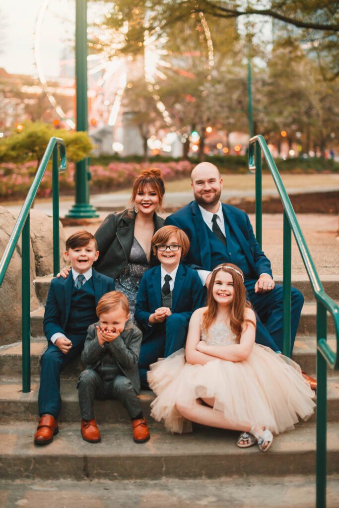 family seated on stairs in formal outfits with Skyview ferris wheel in the background in Atlanta, GA.