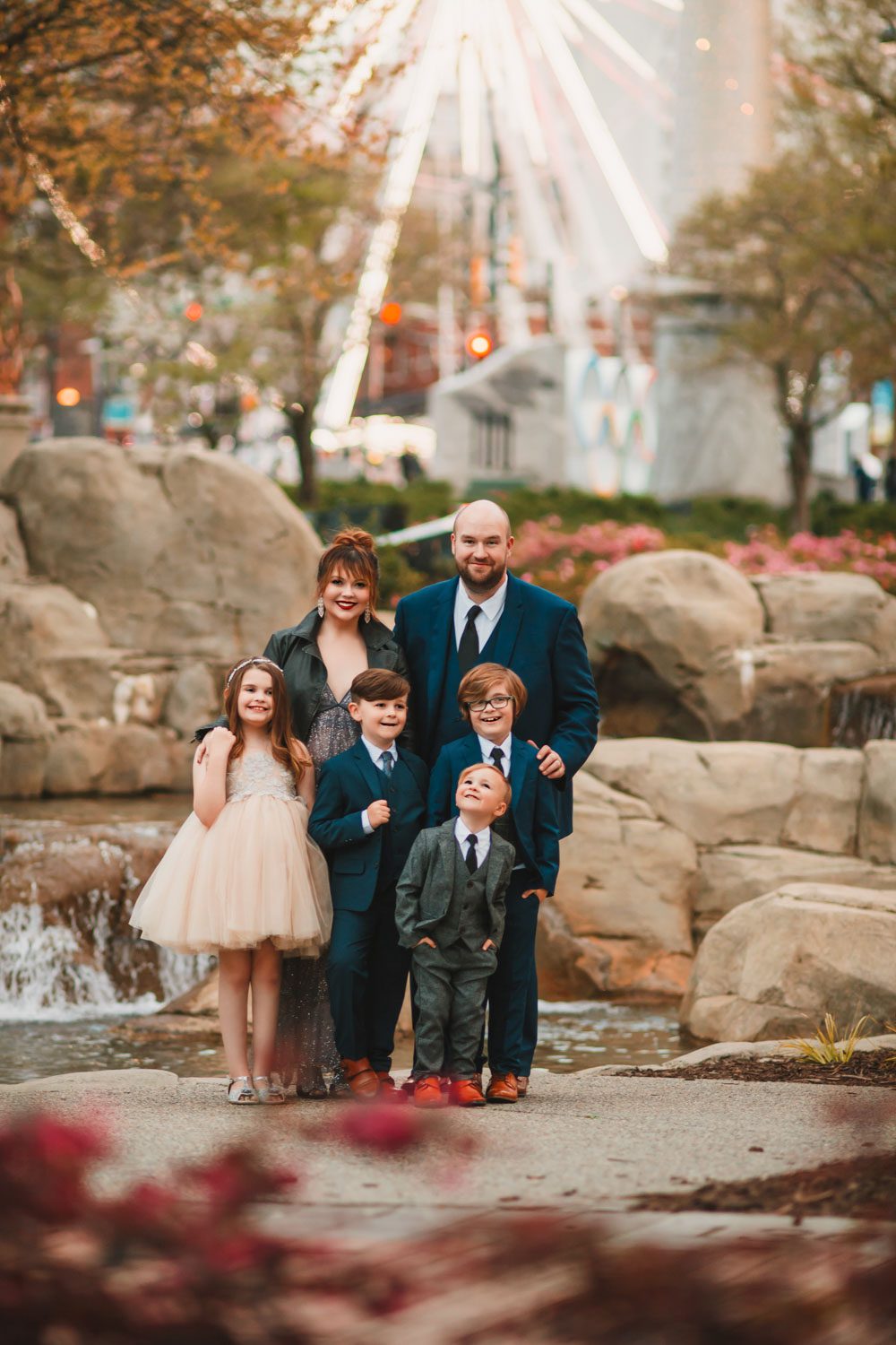 parents standing with four children with the Centennial Olympic Park SkyView Ferris Wheel in the background in Atlanta, GA