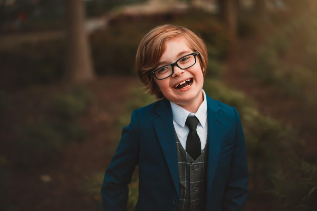 smiling young boy in navy blue tailored suit and tie with glasses