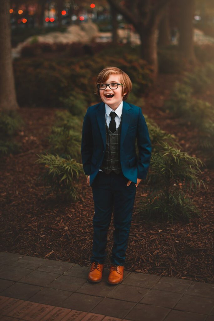 smiling tween boy in blue suit and brown shoes looking off to the side and laughing