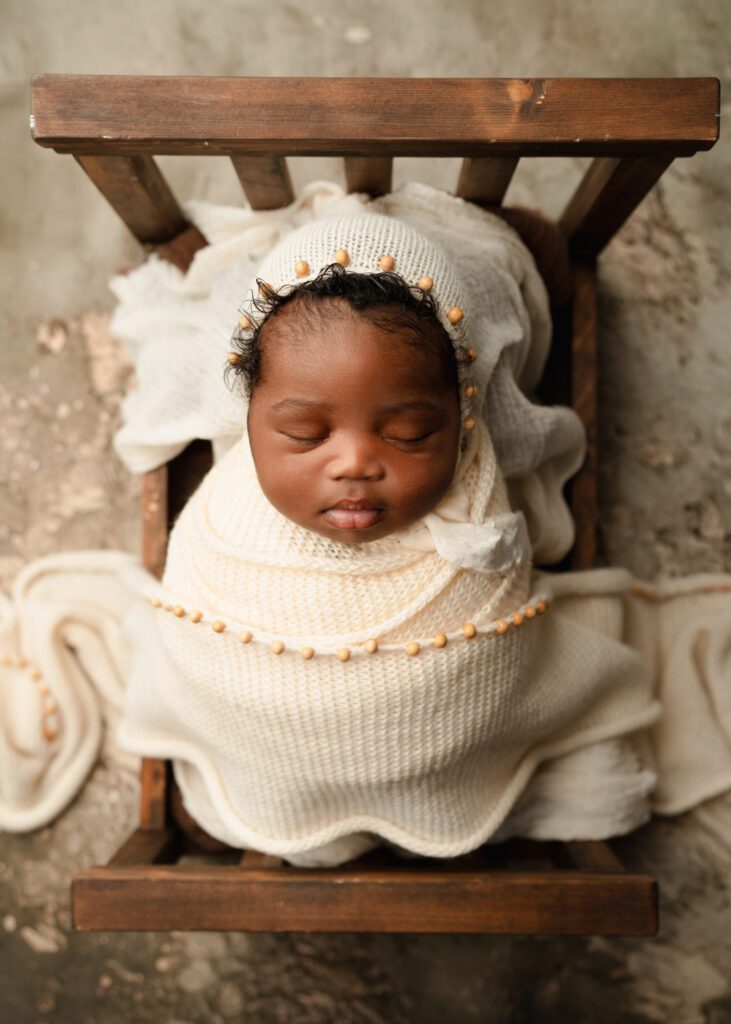 four week old Swaddled newborn baby in a white crochet wrap and matching bonnet in wood bed prop.