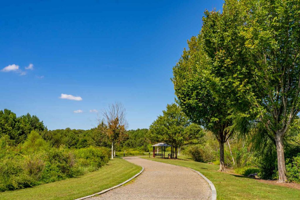 Winding gravel path bordered by trees and green lawns beside a covered seating area at Garrard Landing Park.