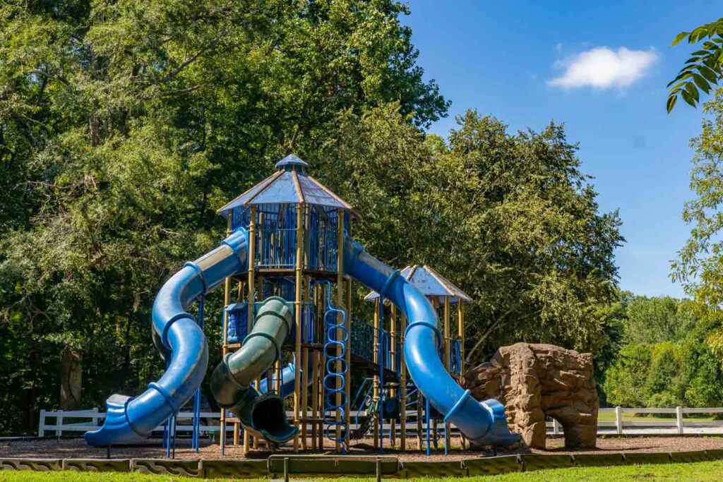 Blue slides, climbing structures, and a rock play feature surrounded by trees at Garrard Landing Park.