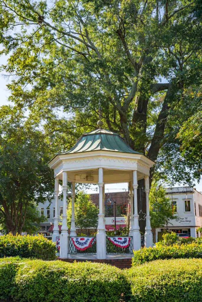 White gazebo with a green roof surrounded by trees and flowering gardens in Glover Park