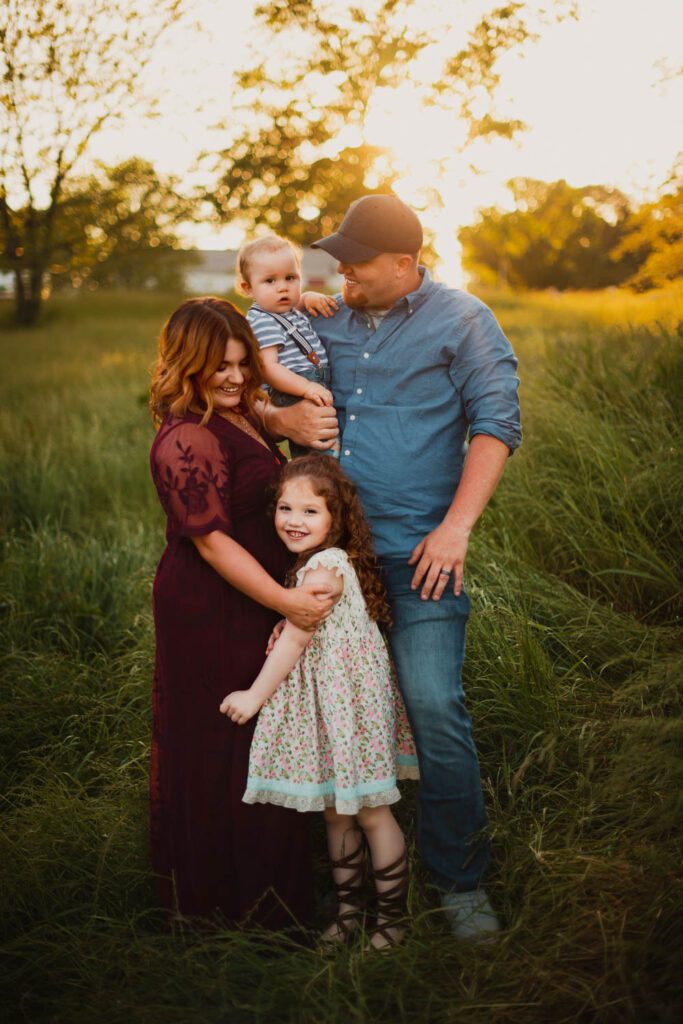 Parents standing with their daughter and baby son in the fields at Cheatham Hill with golden light behind them.