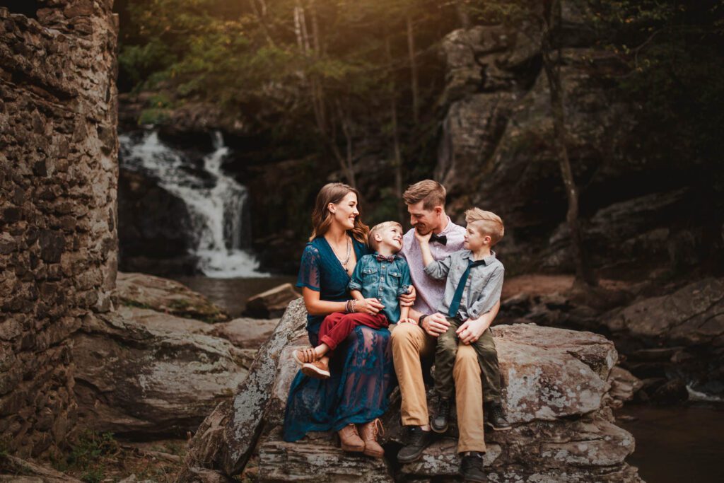 Parents with two sons on a large rock next to stone ruins with Cochran Mill Falls in the background in Chattahoochee Hills, GA.