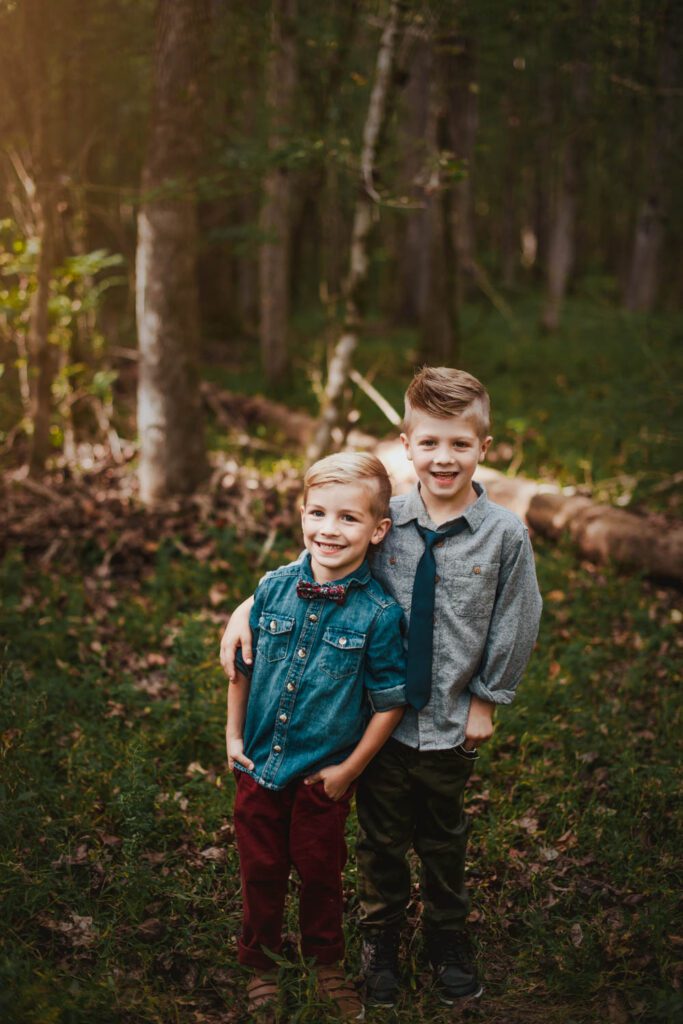 Two brothers standing side by side on a wooded trail near tall trees photographed by peachtree city family photographer
