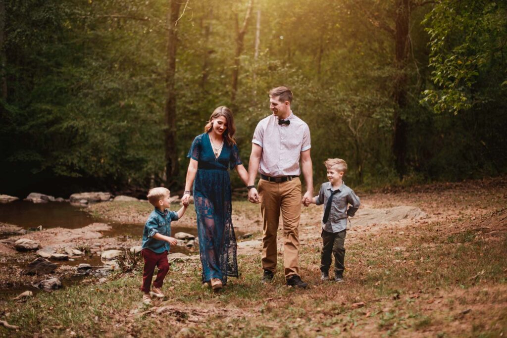 Parents walking hand in hand with their two sons near creek photographed by Peachtree City family photographer.