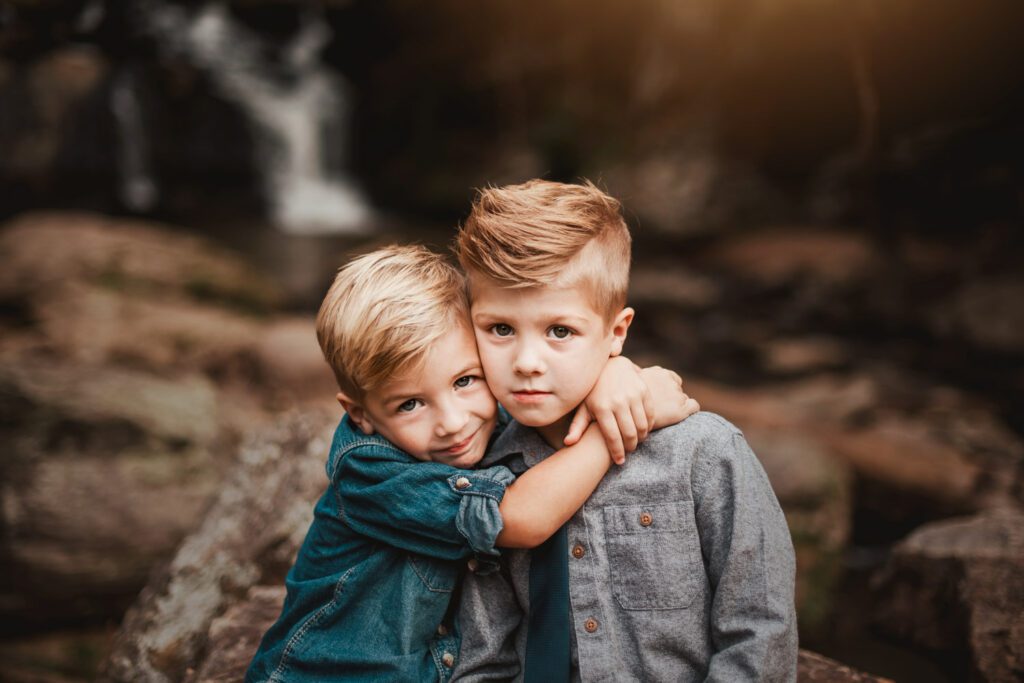 Two brothers hugging closely together with a softly blurred waterfall and rocks behind them.