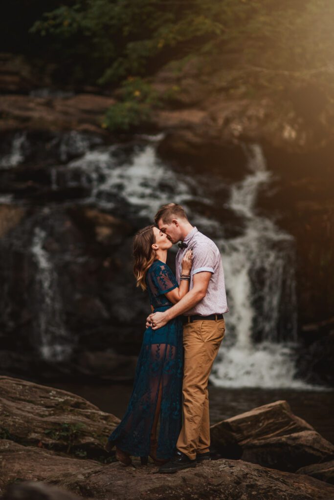 Mom and dad kissing on rocks with Cochran Mill Falls waterfall in the background in Chattahoochee Hills GA