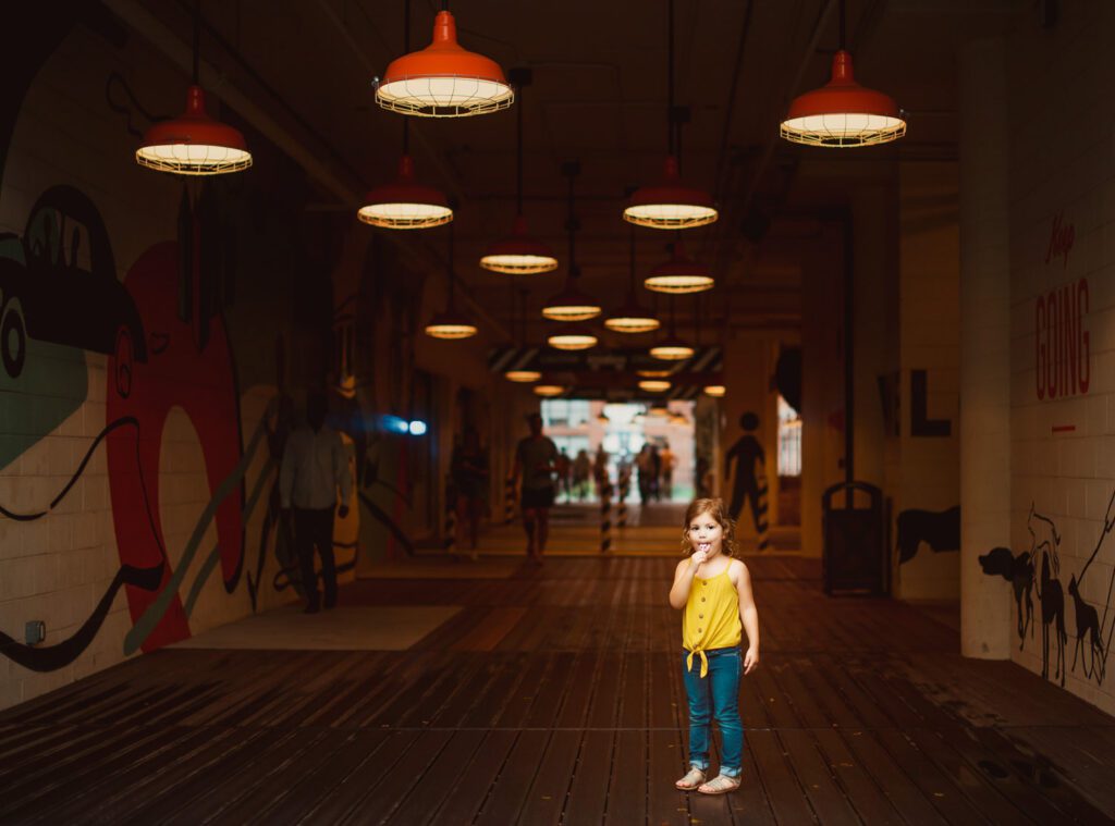 young girl standing in breezeway with Ponce City Market vintage orange pendant lights in the background in Atlanta, GA.