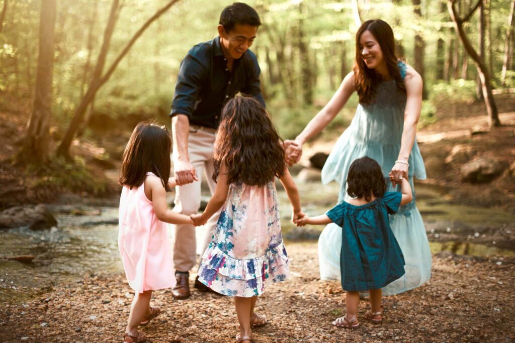 Parents holding hands with their three daughters beside the shallow rocky creek at Vickery Creek in Roswell, GA.