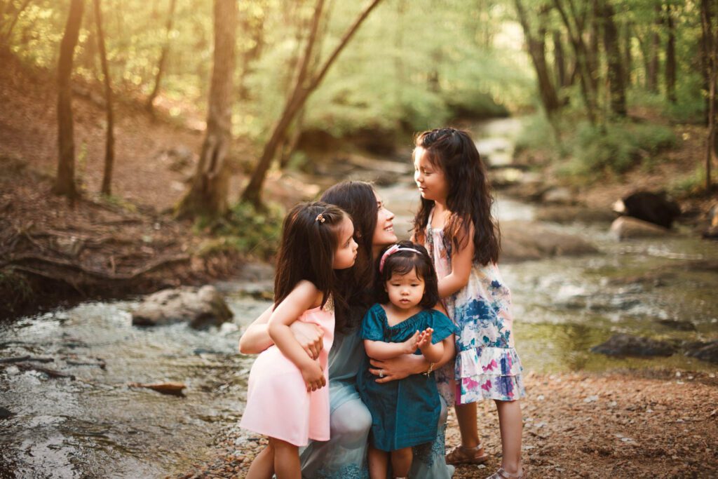 Mom standing beside the creek with her three daughters gathered closely around her.