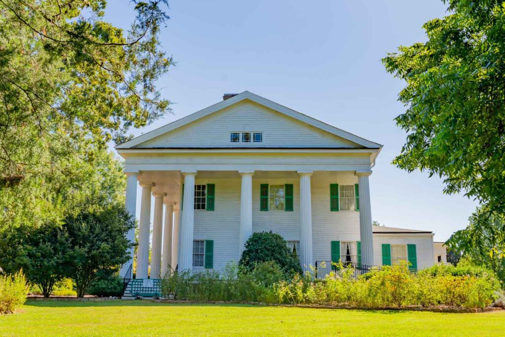 Front view of Barrington Hall in Roswell, GA, with white columns, green shutters, gardens, and a broad lawn.