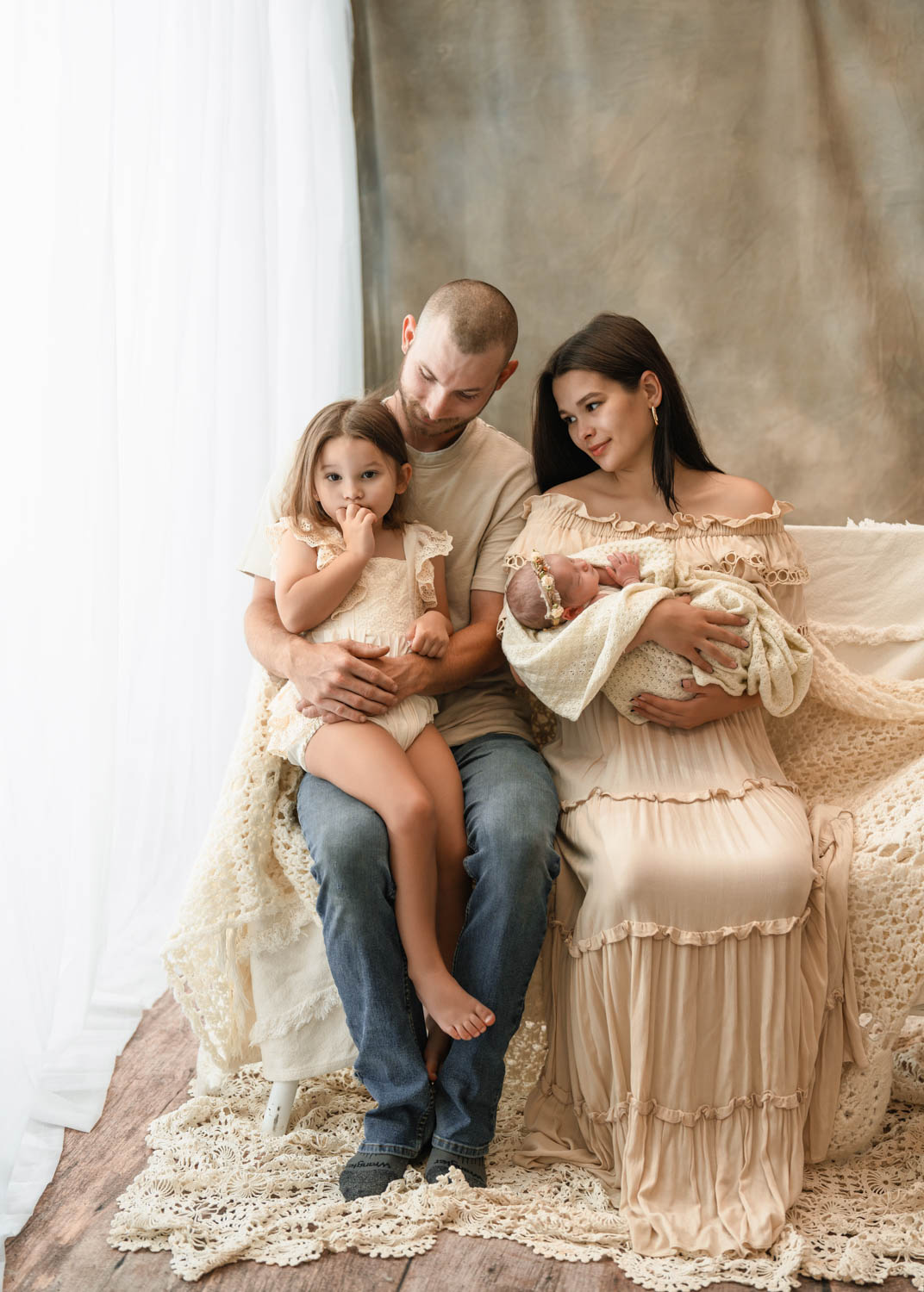Family of four seated together as mom holds their newborn baby photorgraphed by rosewell newborn photographer